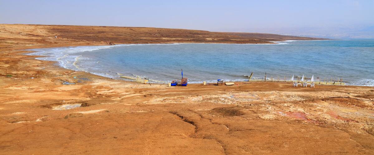A coastal landscape with a sandy beach, a small boat, and a few white structures near the water.