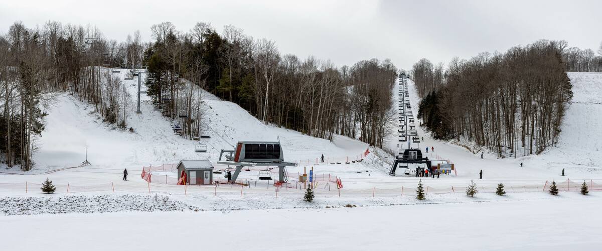 A snow-covered ski slope with a ski lift, trees, and a small cabin.