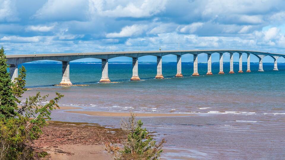 A long bridge over a body of water with a beach in the foreground.
