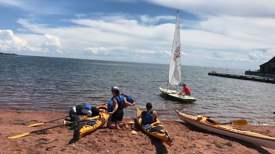 A sandy beach with kayaks and a sailboat.