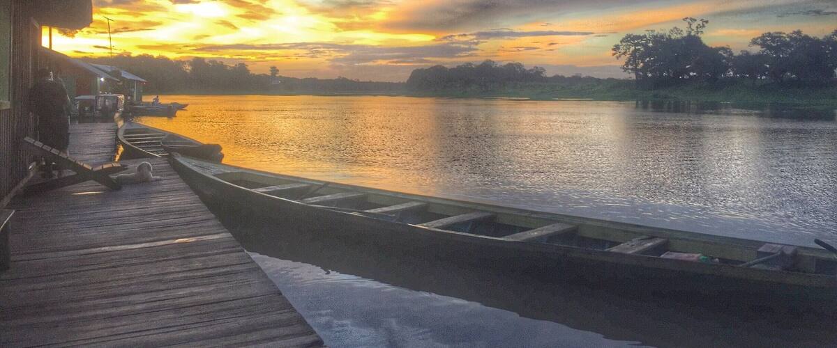 A wooden dock extending into a calm river at sunset with boats docked.