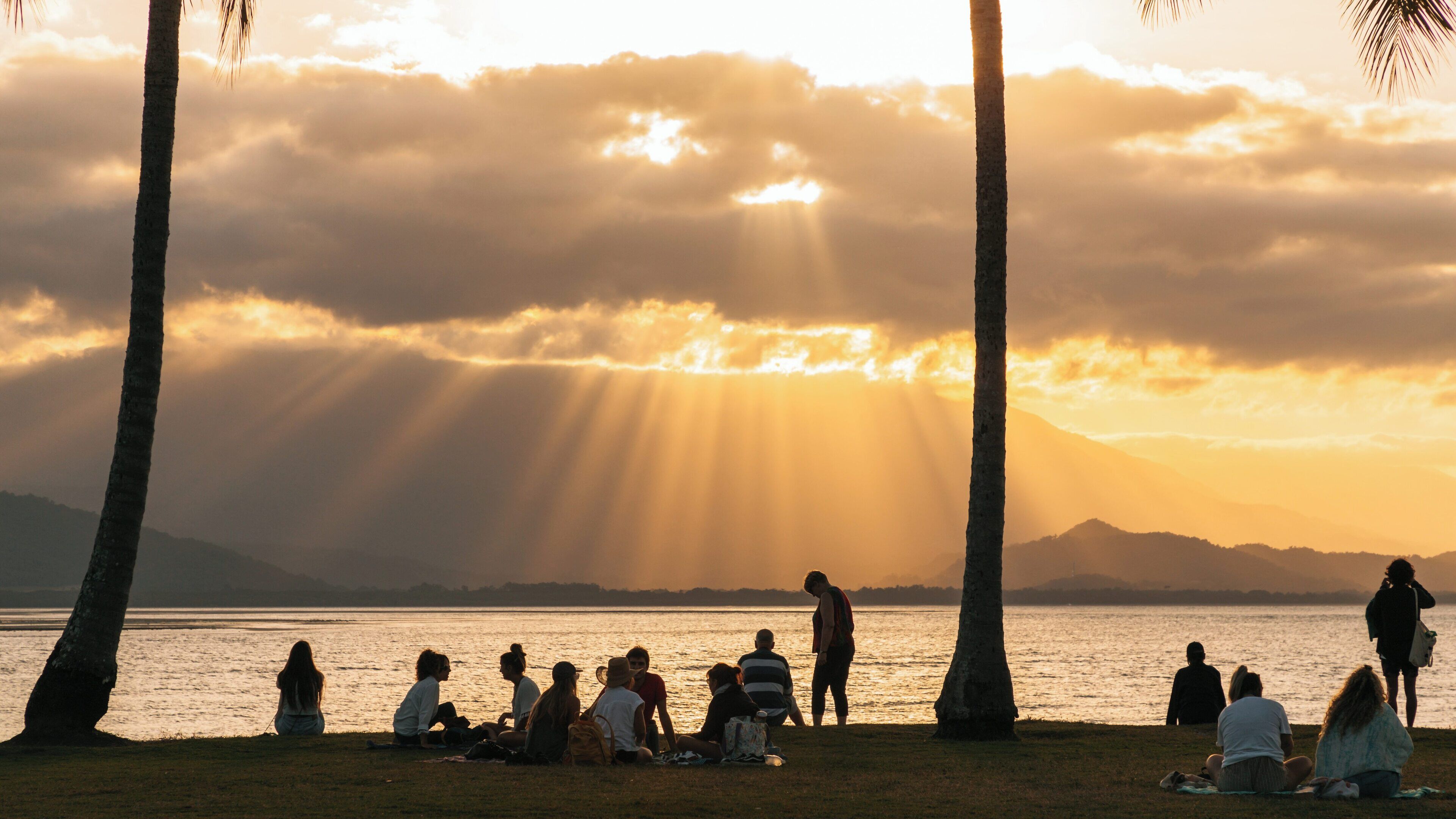 Sunset gathering at Anzac Park in Port Douglas, Queensland with golden rays illuminating the landscape and people enjoying the view