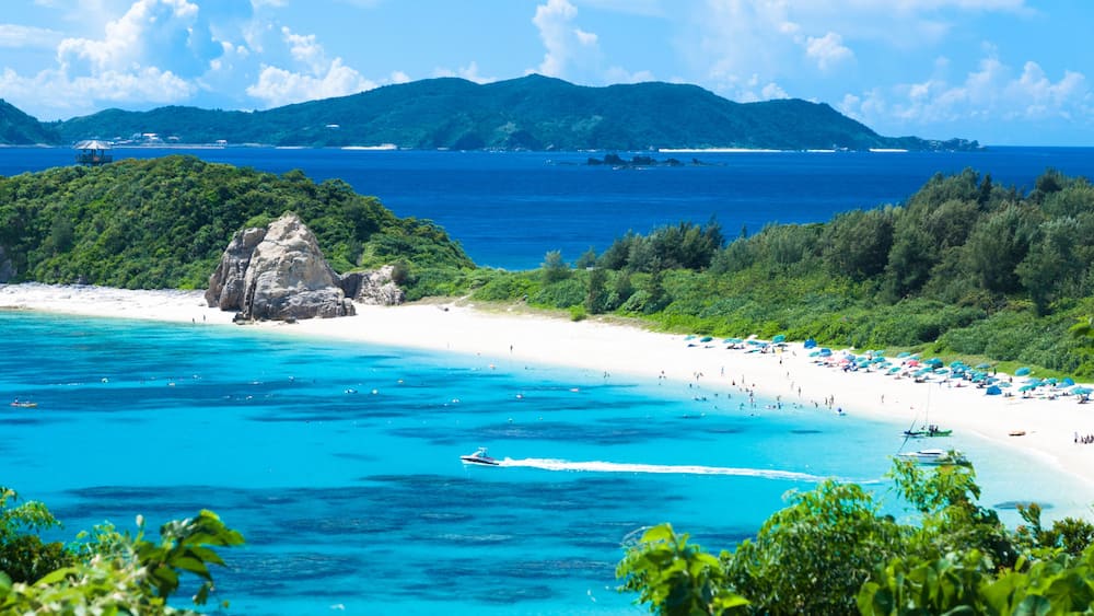 A beach with clear turquoise waters, a rocky outcrop, and lush greenery.
