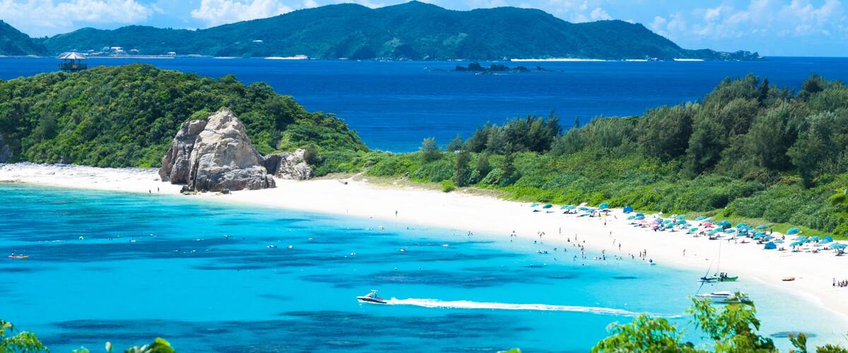 A beach with clear turquoise waters, a rocky outcrop, and lush greenery.