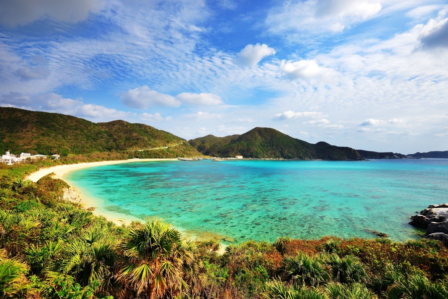 A coastal landscape with a sandy beach, turquoise waters, and lush green hills.