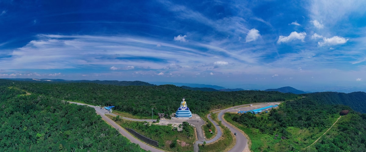 A large blue and white pagoda surrounded by lush green mountains and winding roads.