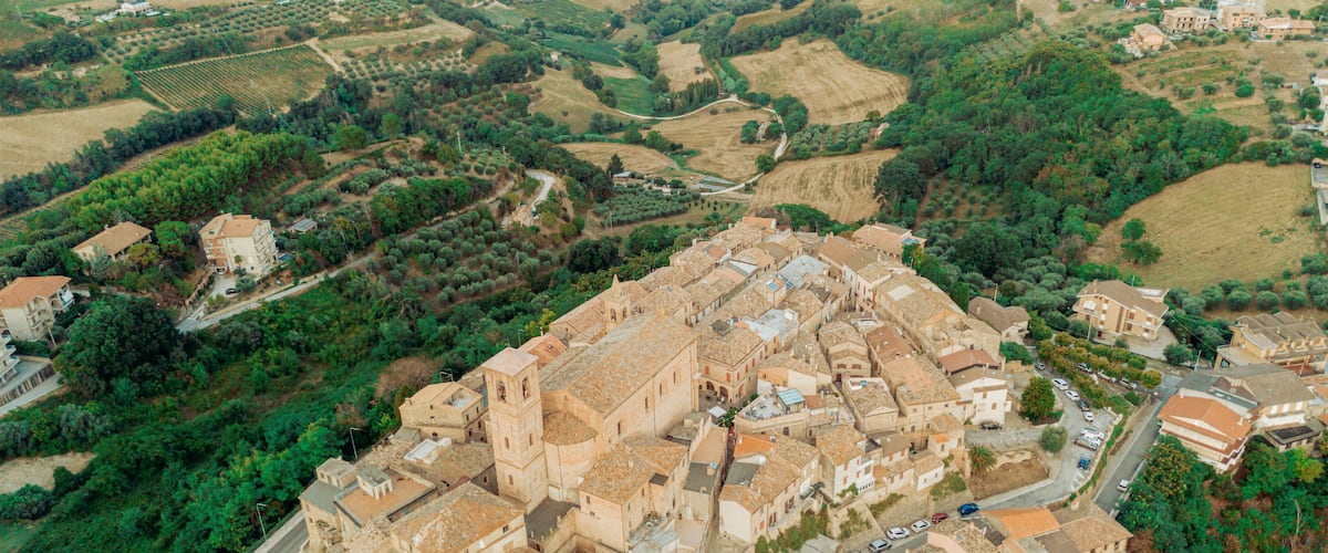 Vista aérea de un pueblo histórico con una iglesia destacada, rodeado de colinas ondulantes y viñedos.