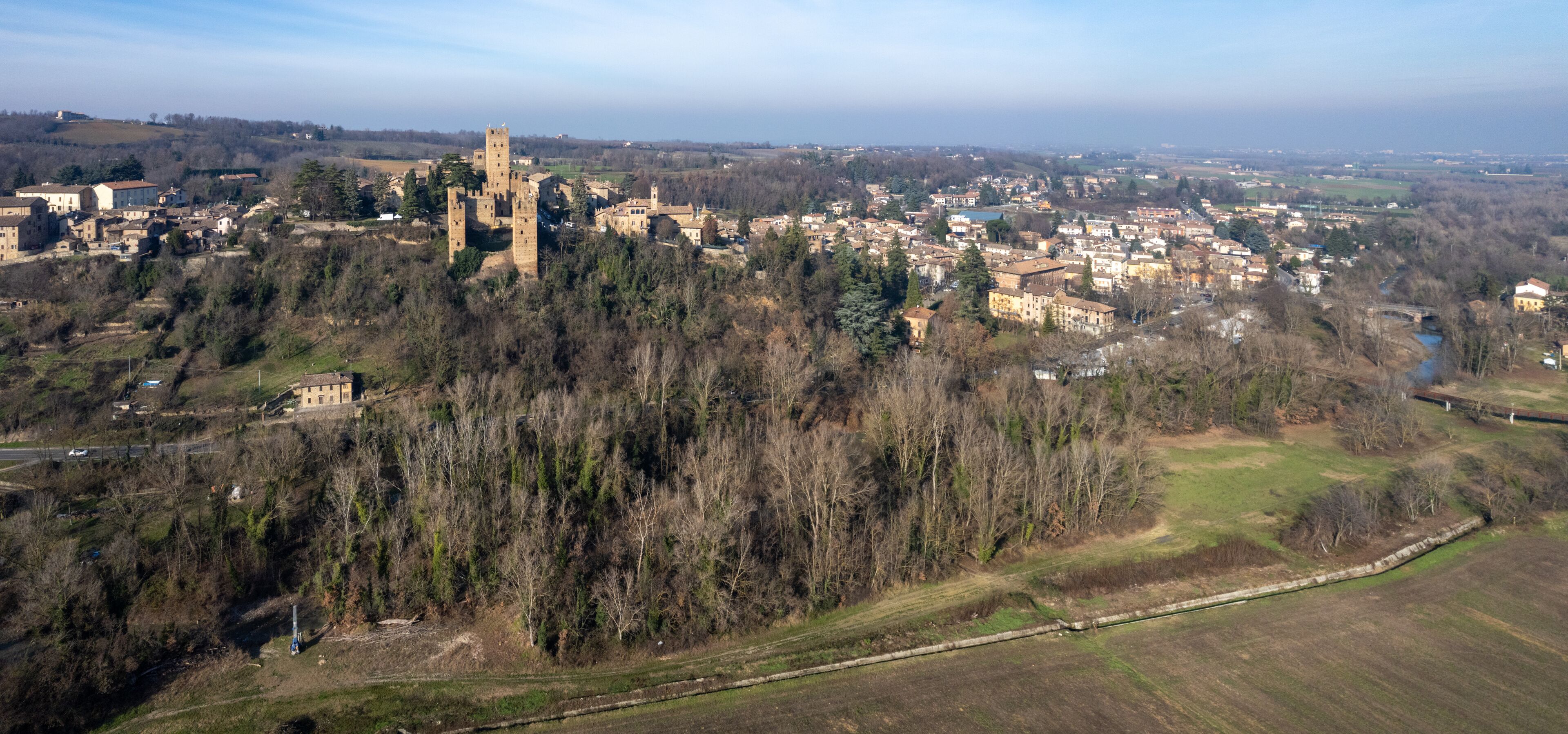 A medieval castle surrounded by a town and forested hills.