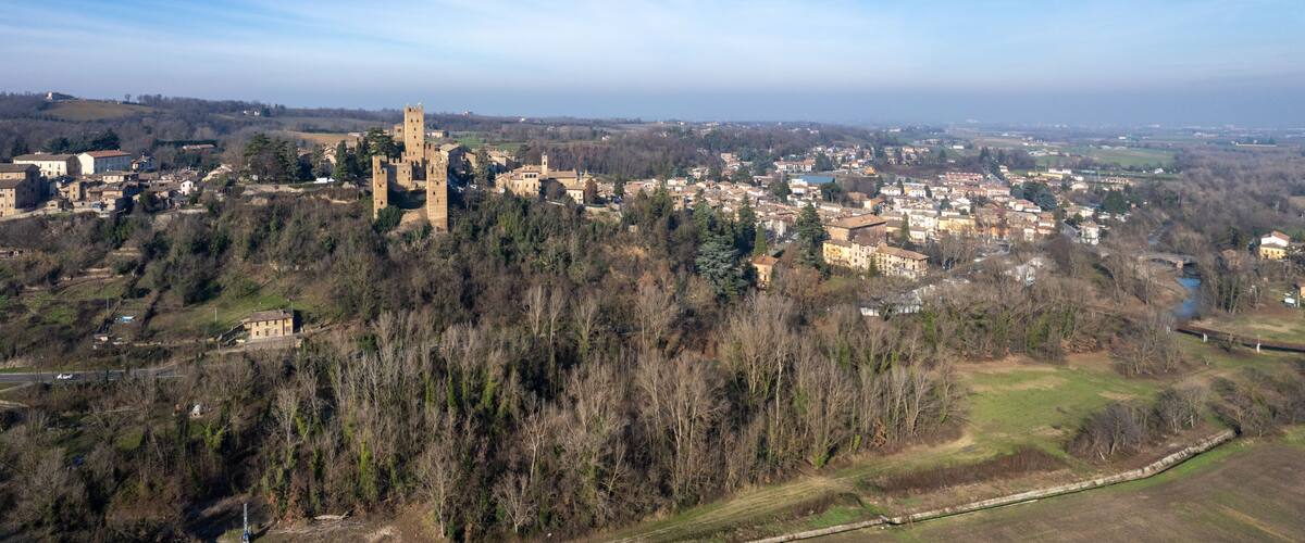 A medieval castle surrounded by a town and forested hills.