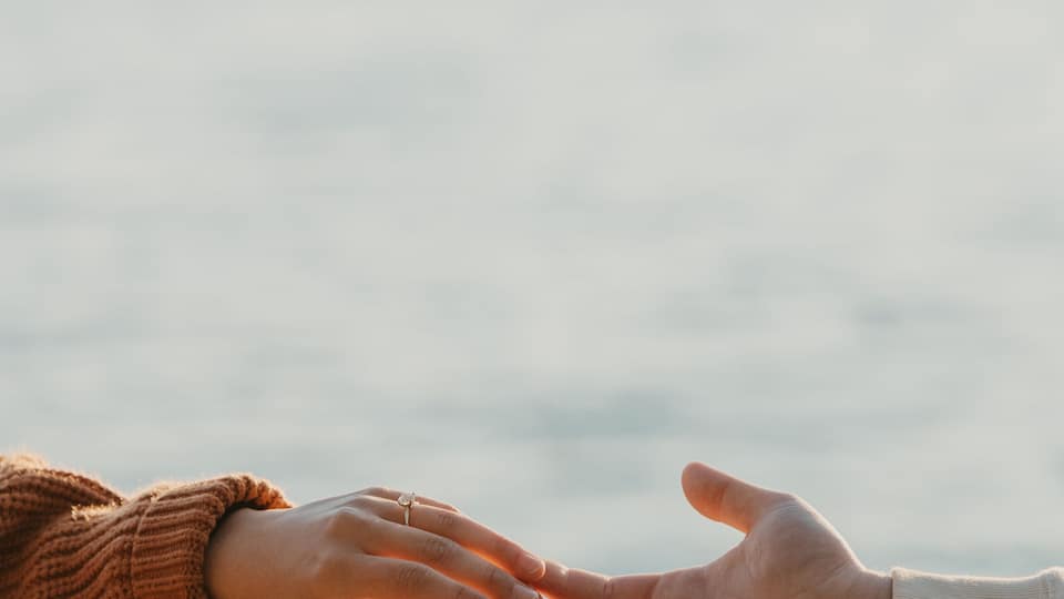 Two hands reaching towards each other over a body of water with a mountain in the background.
