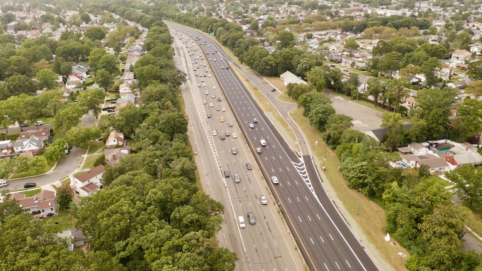 A multi-lane highway with surrounding residential areas and dense tree coverage.