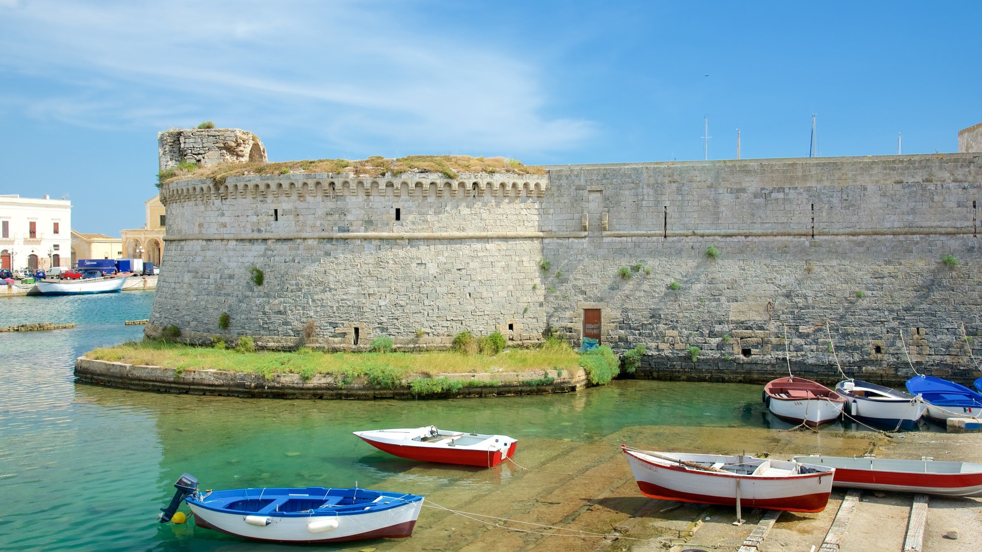 A stone fortification by a calm harbor with several small boats docked.