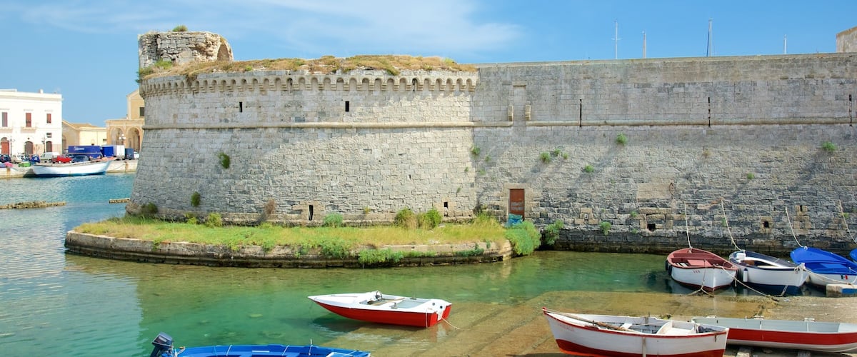 A stone fortification by a calm harbor with several small boats docked.