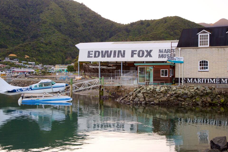 Un muelle con un edificio identificado como 'Edwin Fox Maritime Museum' y un pequeño avión azul y blanco amarrado.