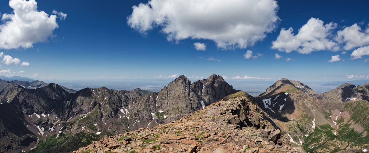 A mountain range with rocky terrain and snow patches under a clear blue sky with scattered clouds.