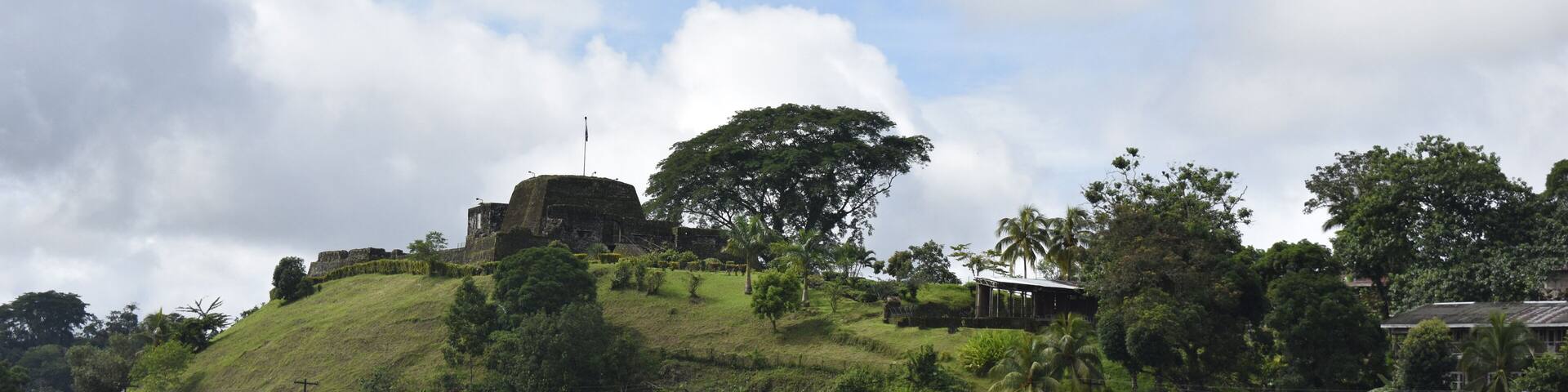 A riverside village with colorful houses, a hilltop fort, and lush greenery.