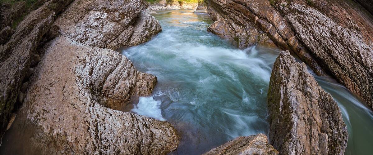 A fast-flowing river surrounded by large rocks and lush greenery.