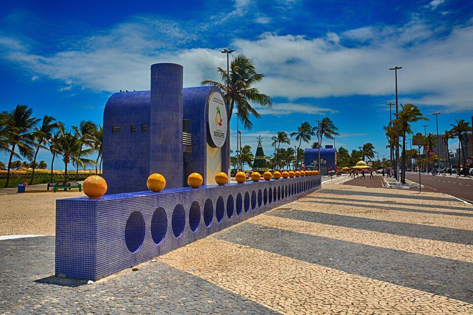 Una estructura de azulejos azules con decoraciones esféricas, palmeras y un cielo despejado.