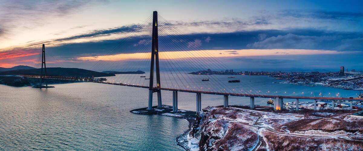 A suspension bridge over a body of water with snow-covered land in the foreground.