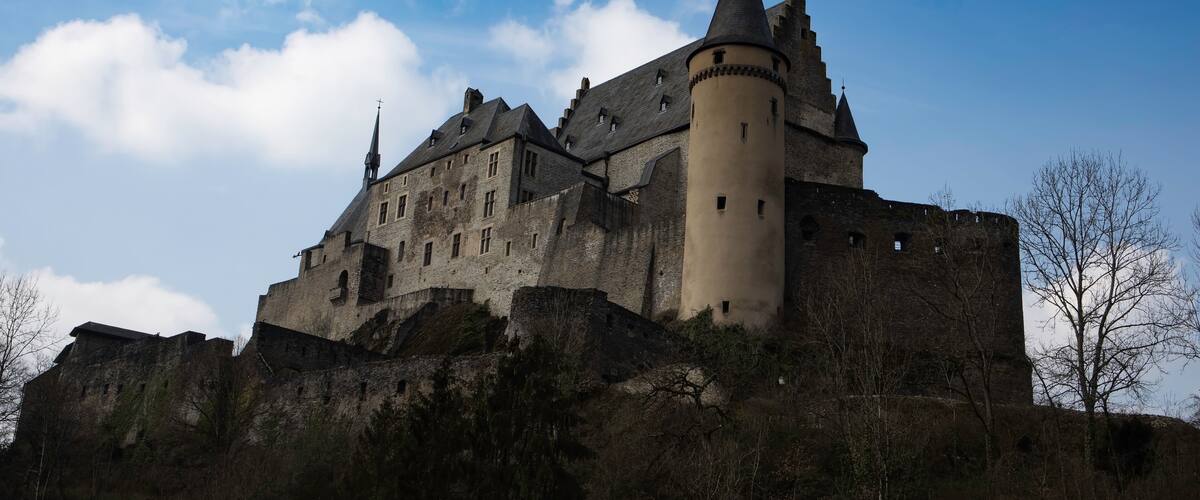 A historic castle with multiple towers and a prominent central tower, surrounded by a hilly landscape.