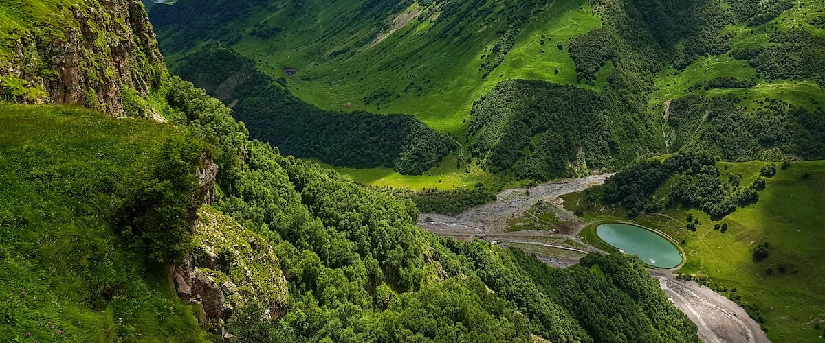 A lush valley with a river, a lake, and steep hills.