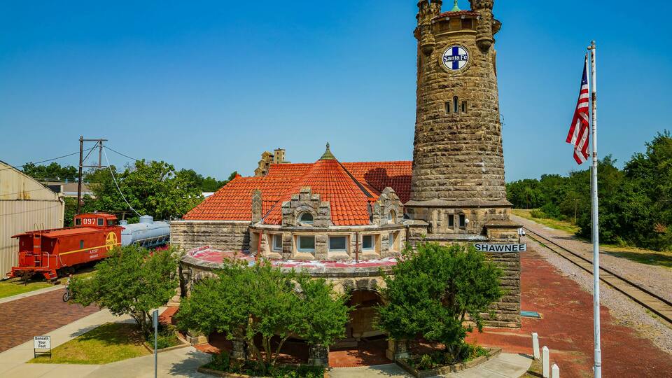A historic building with a clock tower, surrounded by trees and a red-roofed structure.