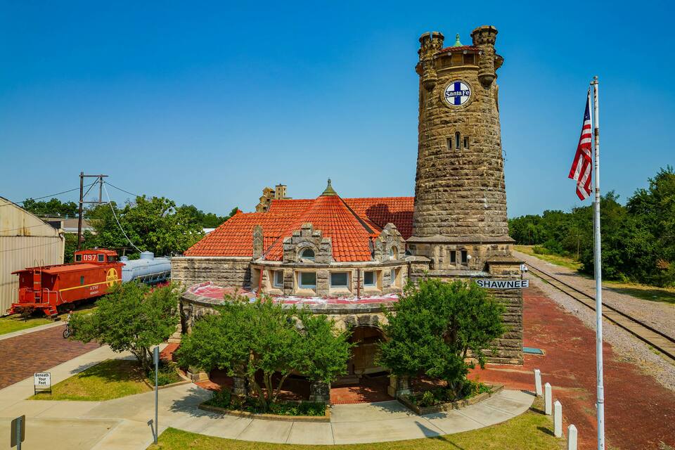 A historic building with a clock tower, surrounded by trees and a red-roofed structure.