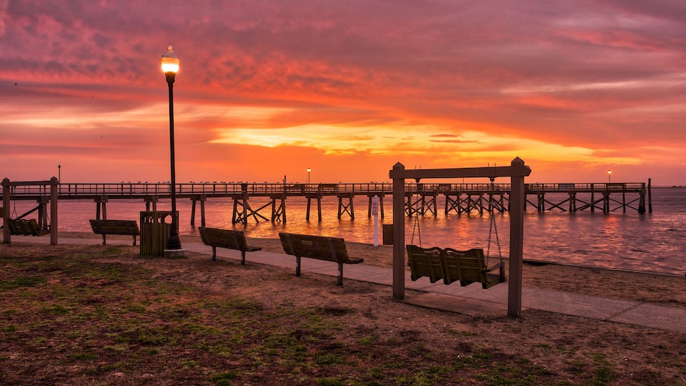 A park with benches and a swing set near a pier at sunset.