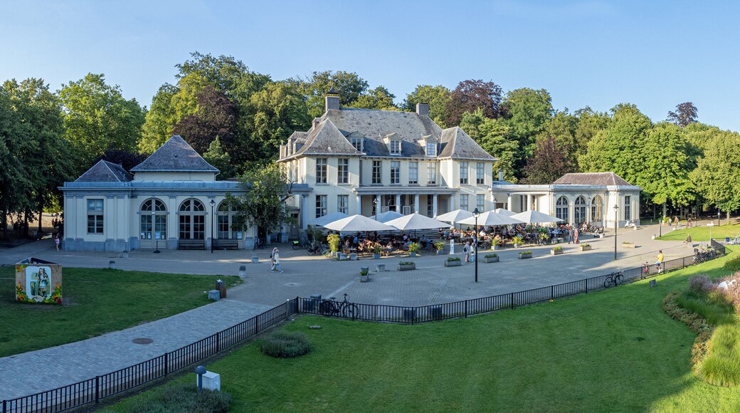 Aerial shot of Rivierenhof castle with umbrellas in front of cafe by a pond in city park Deurne, Antwerp, Belgium. Drone aerial view