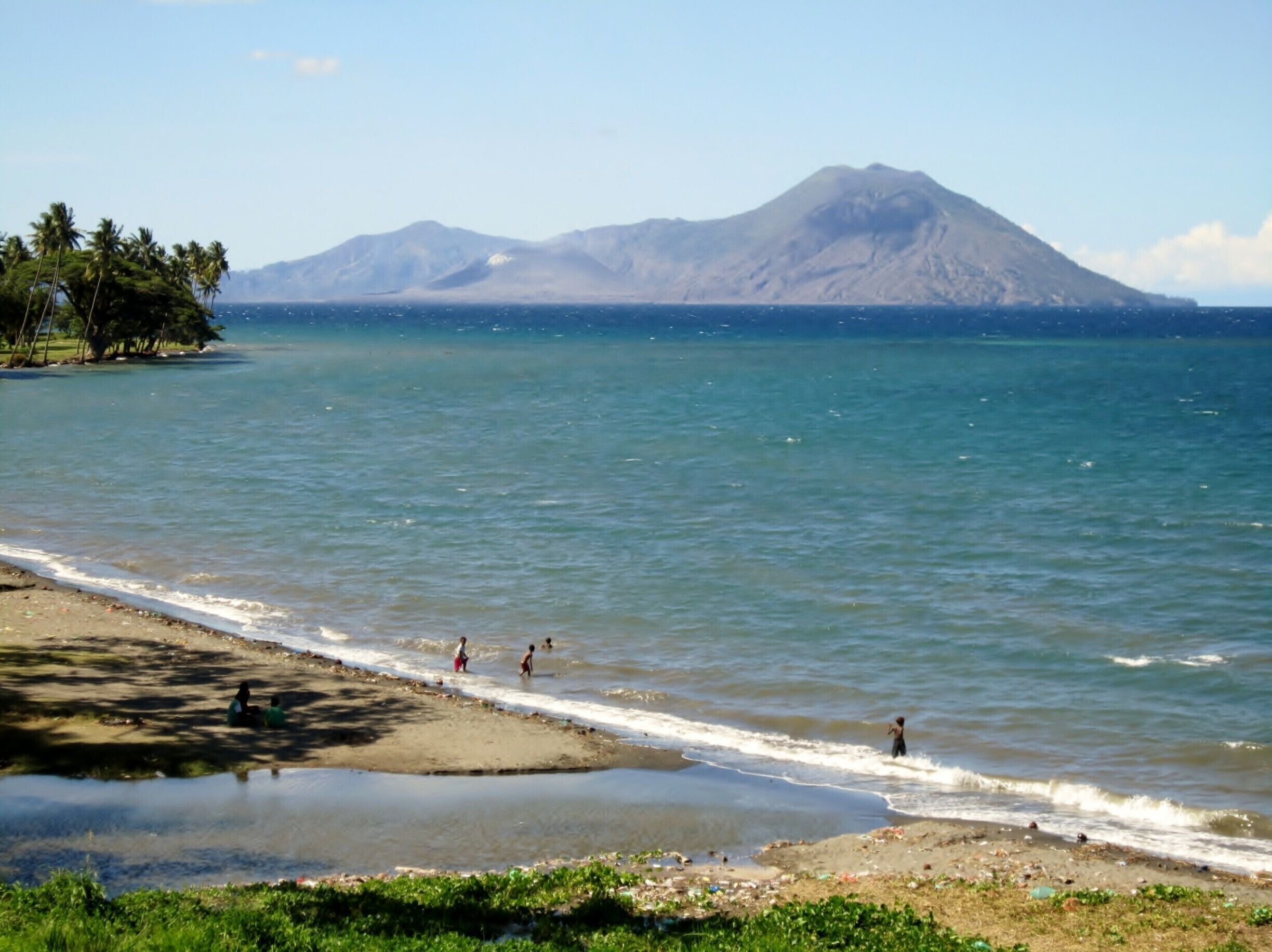 A beach with calm waters, a sandy shore, and a mountain in the background.