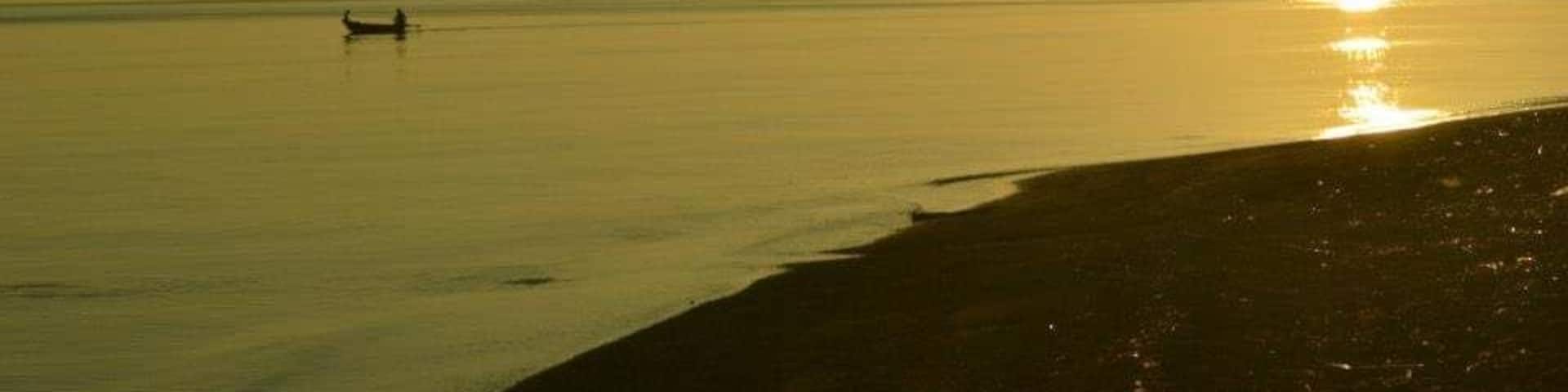 Mar tranquila al atardecer, con un barco a lo lejos y una playa en primer plano.