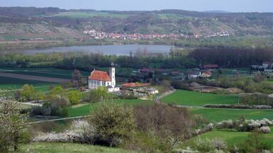 A church with a red roof, a river, and a town in the background.