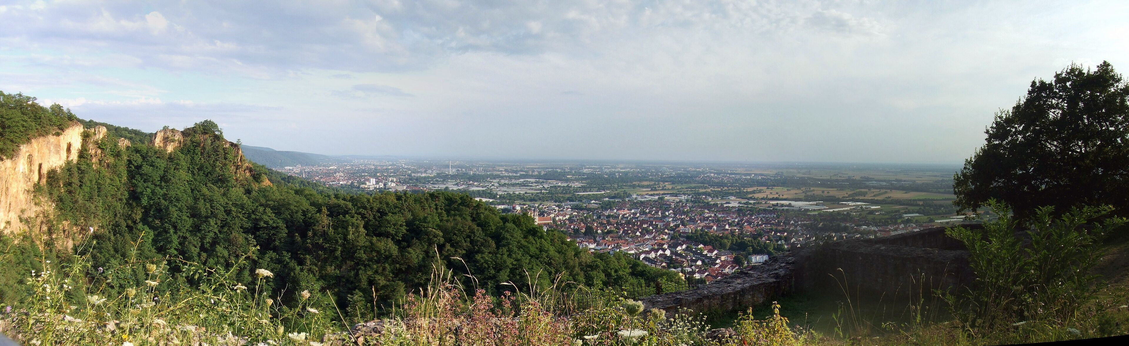 A panoramic view of a town nestled in a valley, surrounded by forested hills and cliffs.