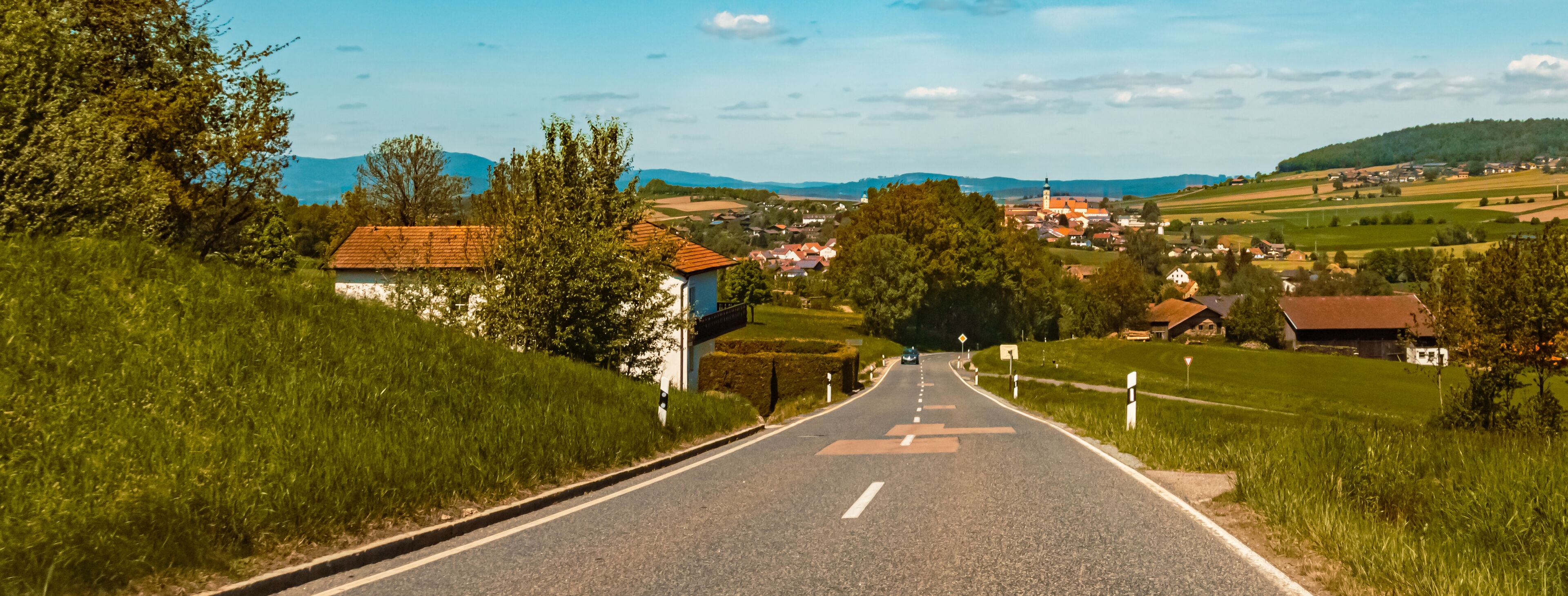A rural road leading to a village with houses and a church.