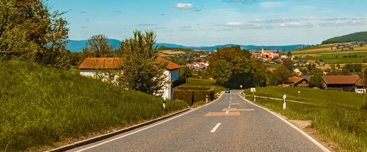 A rural road leading to a village with houses and a church.