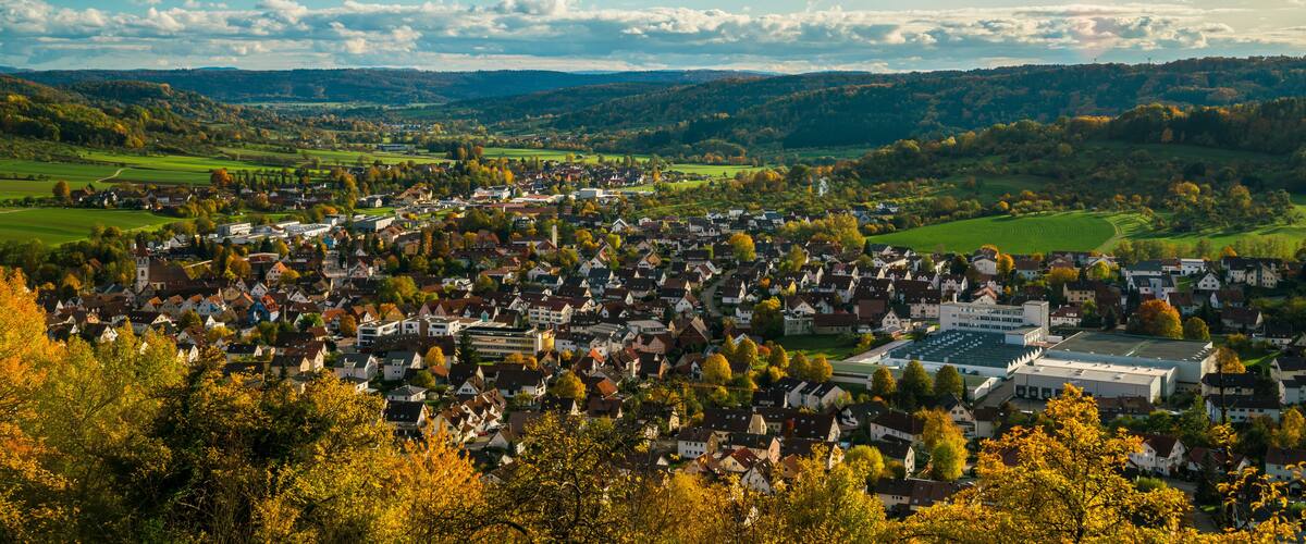A town nestled in a valley with rolling hills in the background, surrounded by autumn-colored trees.
