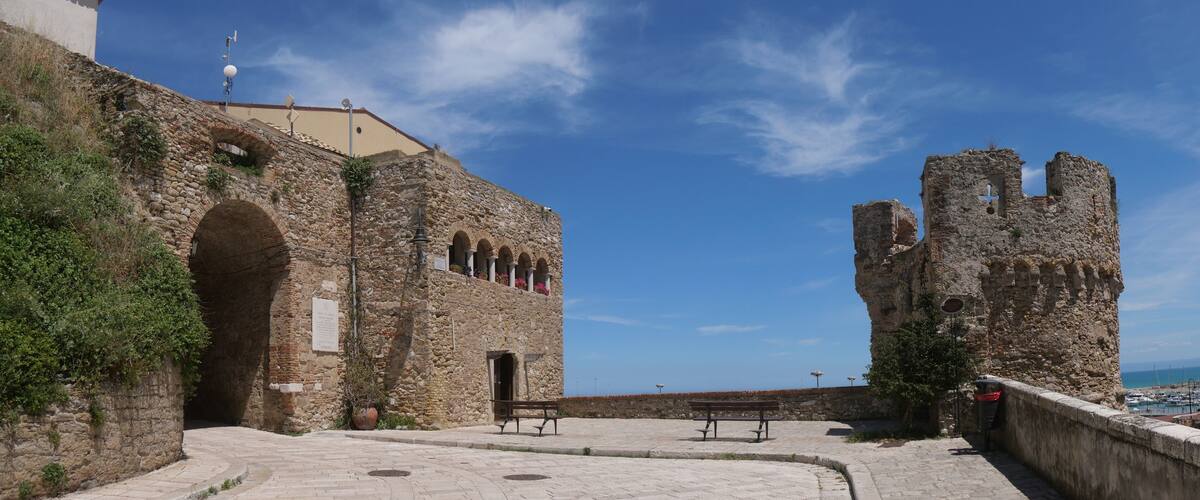 A historic stone building with arches and a tower, overlooking a coastal area.