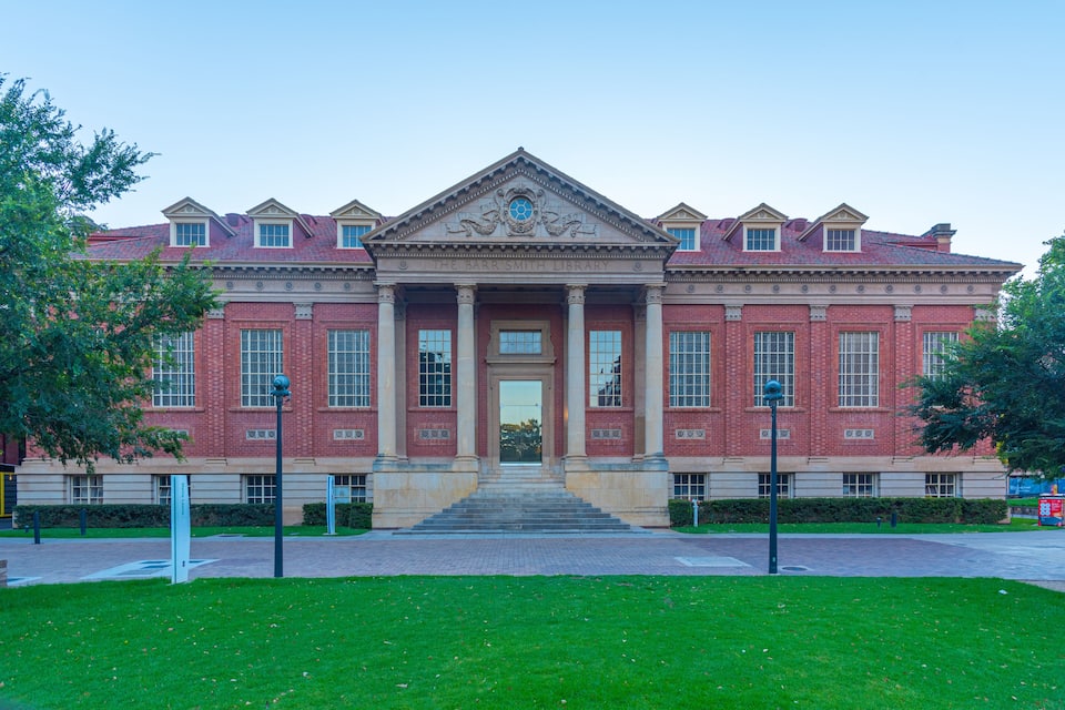A large brick building with a central entrance, columns, and a triangular pediment.