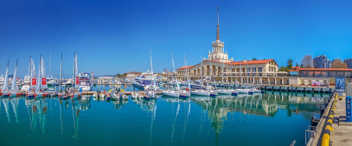 A marina with numerous sailboats docked, a prominent tower, and a mix of historic and modern buildings.