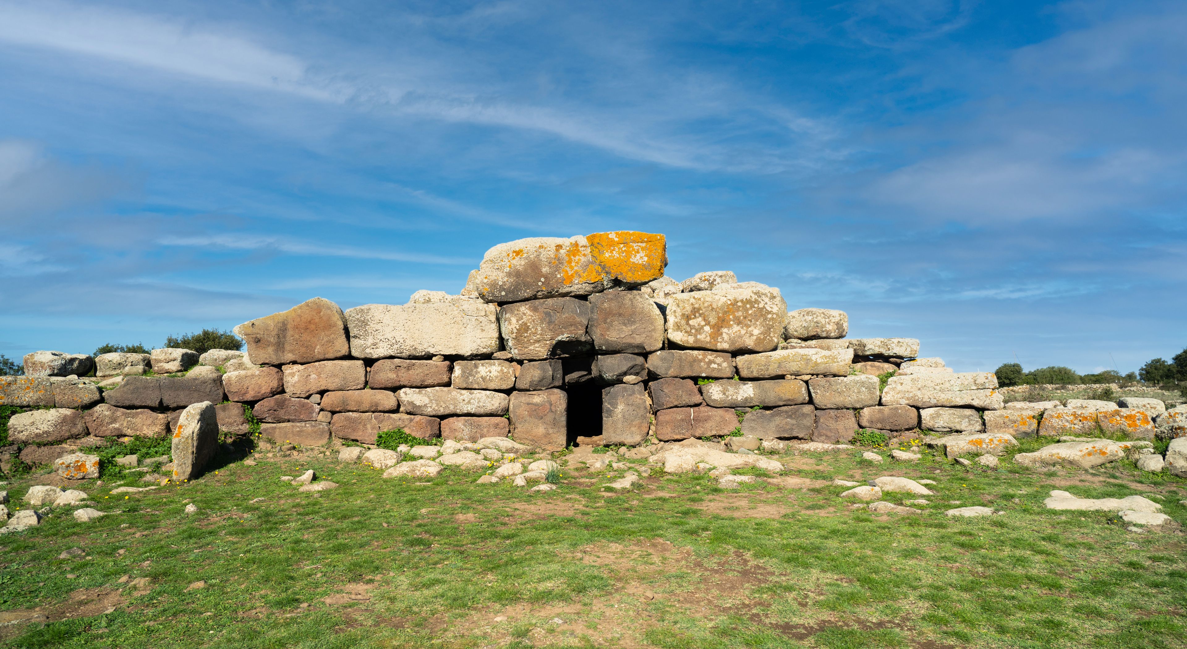 Estrutura de pedra com uma porta central, rodeada por relva e rochas.