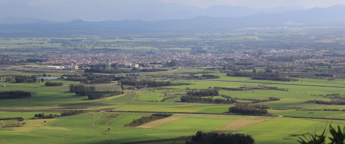 A panoramic view of a rural landscape with fields, a small town, and distant mountains.