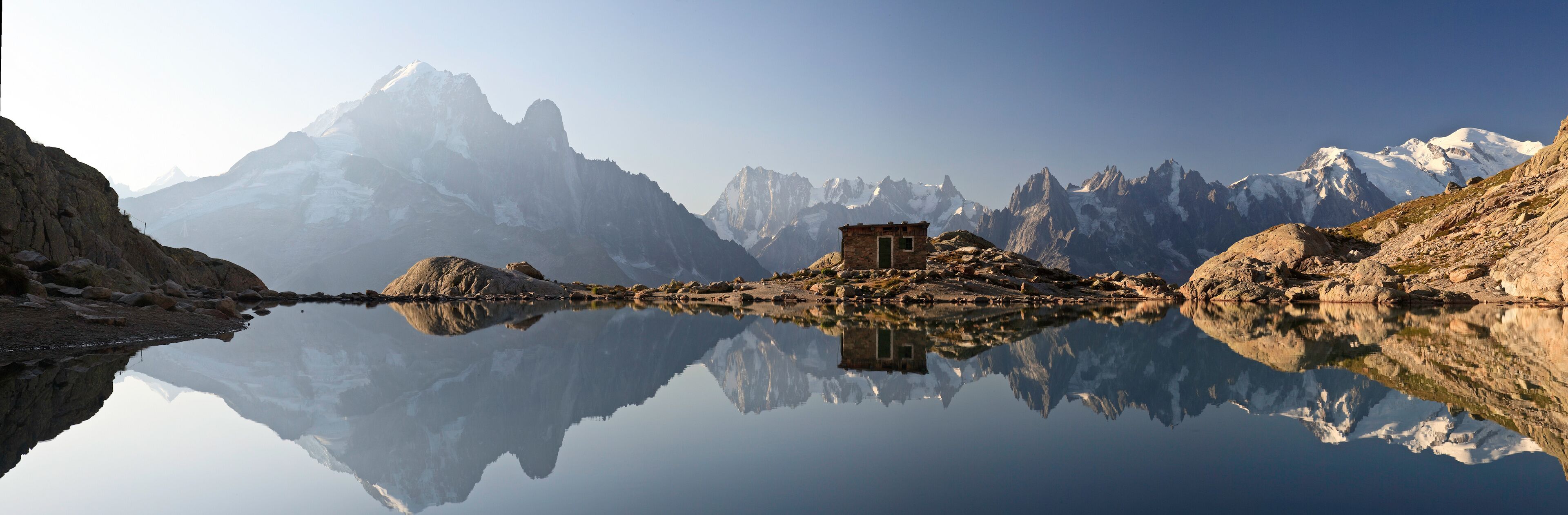 A mountain lake with a small stone building in the center, surrounded by rugged peaks and clear reflections.