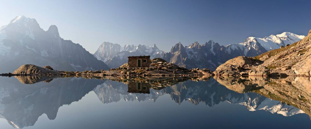 A mountain lake with a small stone building in the center, surrounded by rugged peaks and clear reflections.