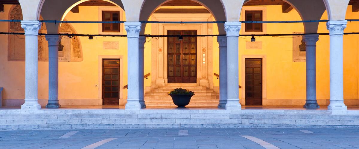 A building with three arched doorways, each with a wooden door and a potted plant in front.