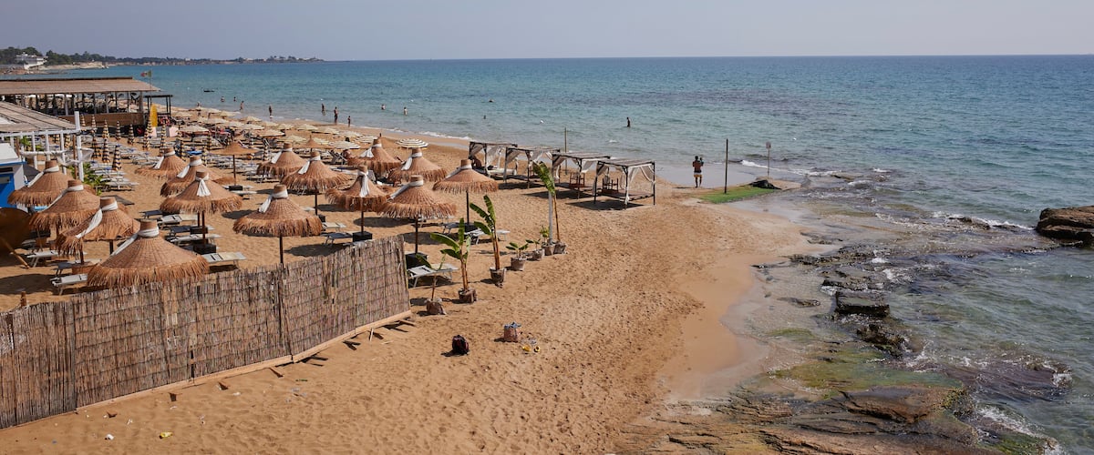 A beach with thatched umbrellas, lounge chairs, and a rocky shoreline.