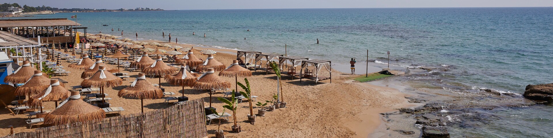 A beach with thatched umbrellas, lounge chairs, and a rocky shoreline.
