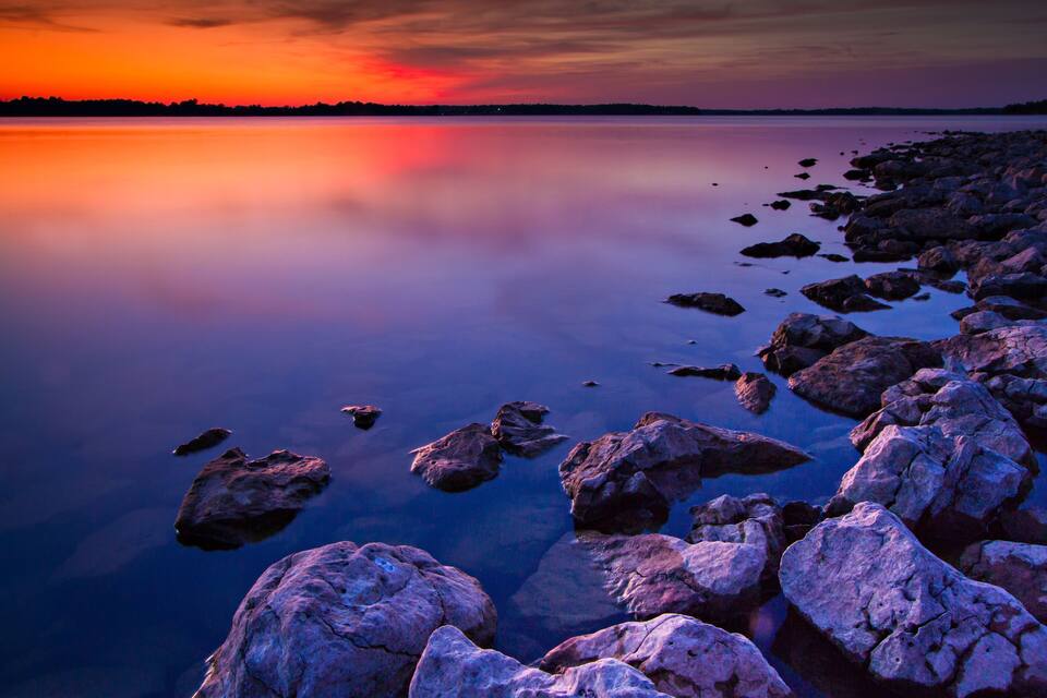 A sunset over a calm lake with rocky shores.