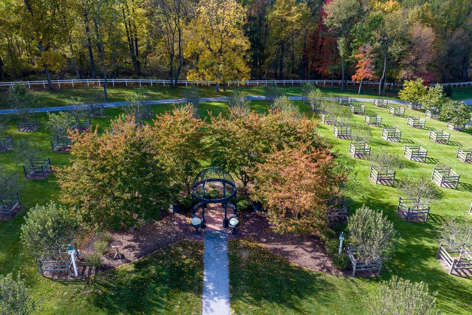 An aerial view of a cemetery with a central circular monument surrounded by trees and a white fence.