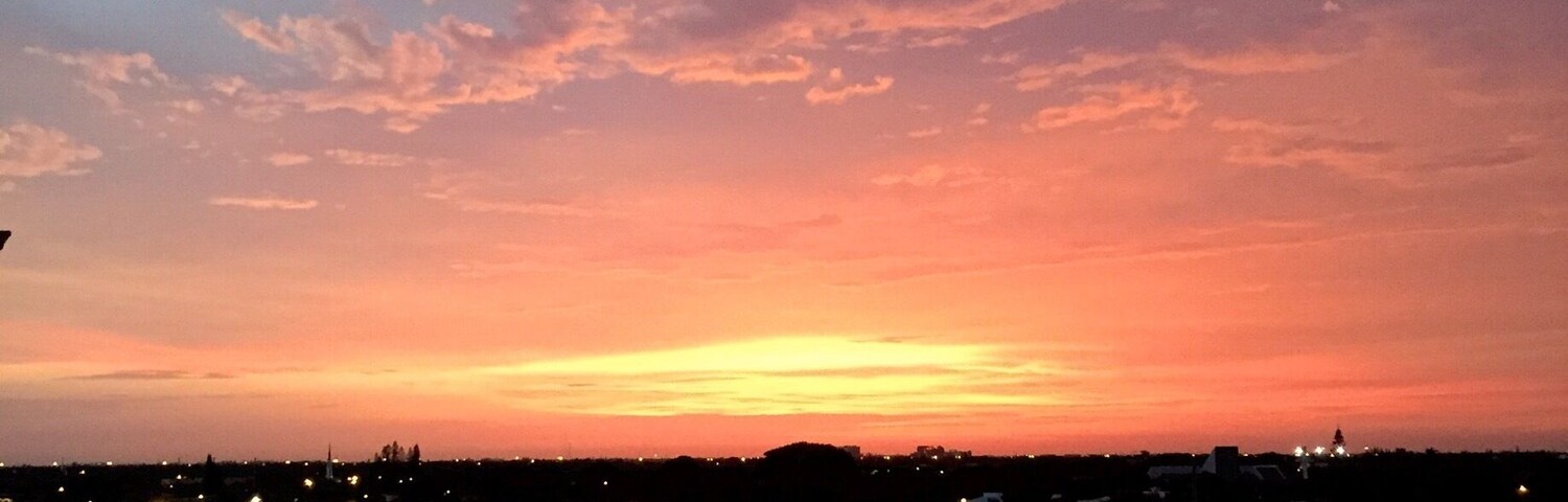 Ein Sonnenuntergang über einer Skyline mit beleuchteten Gebäuden und einem Fluss im Vordergrund.