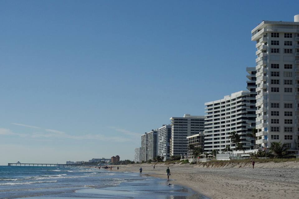 A beach with a pier, high-rise buildings, and palm trees.